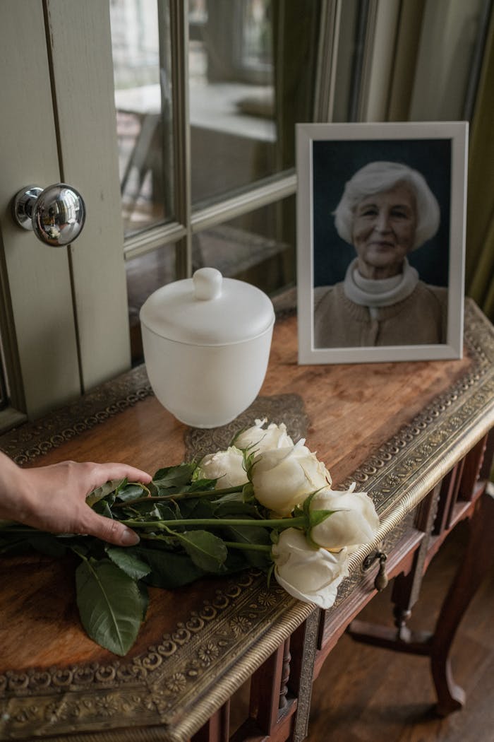 A serene memorial setup with an urn, a photo of a senior woman, and white roses.