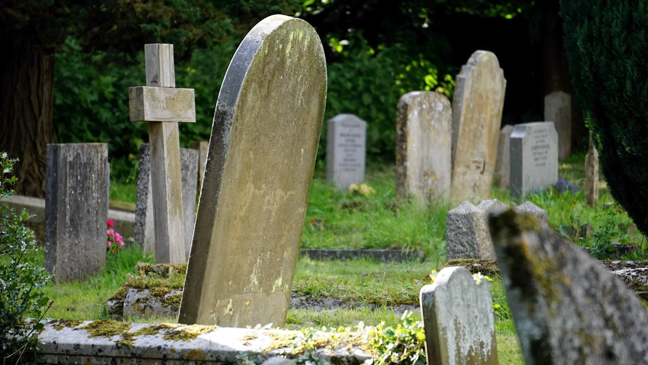 heros-img Weathered tombstones in a tranquil cemetery surrounded by greenery.